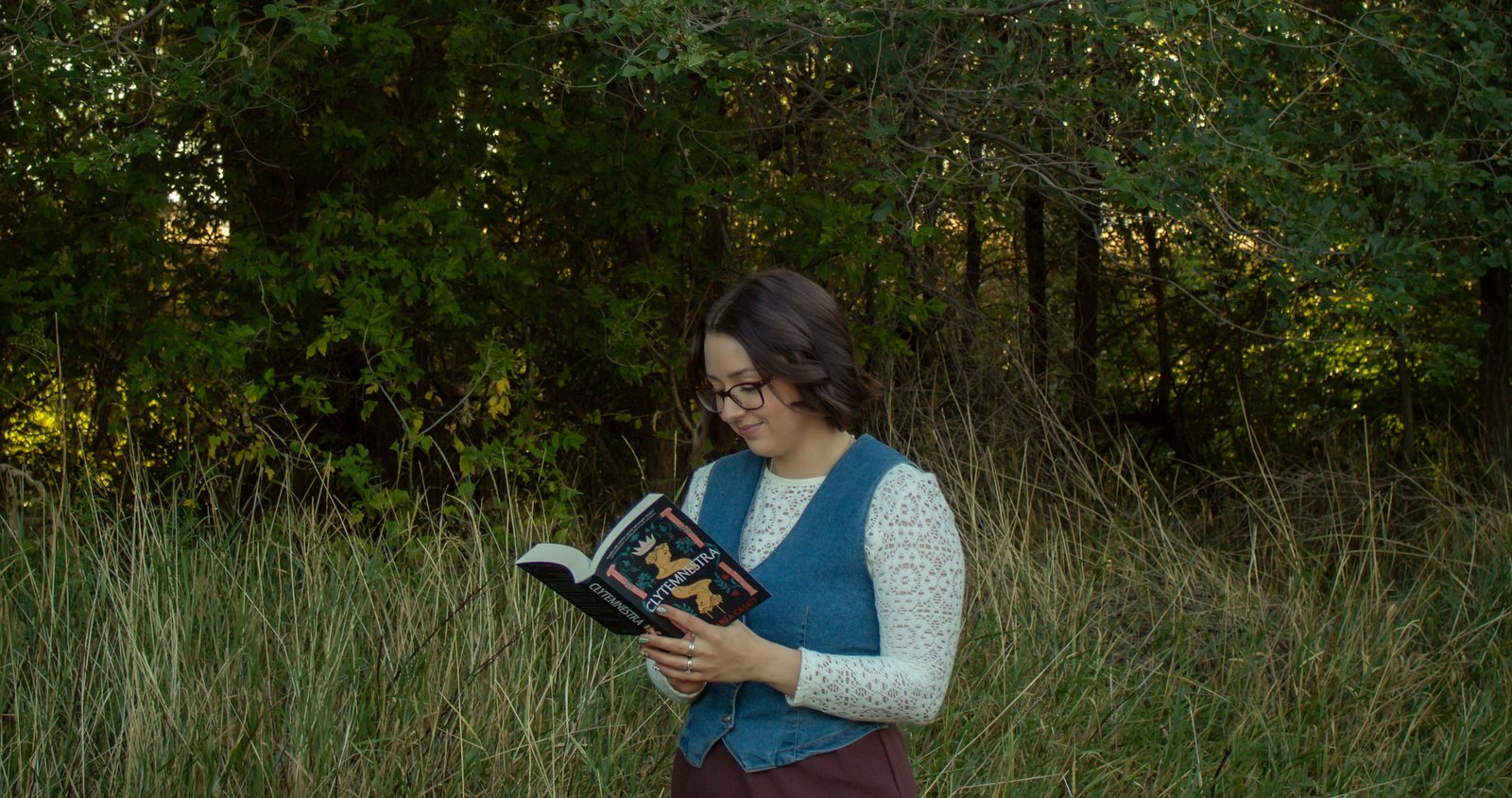 Lynea Millward reading in tall grass at the edge of a wood