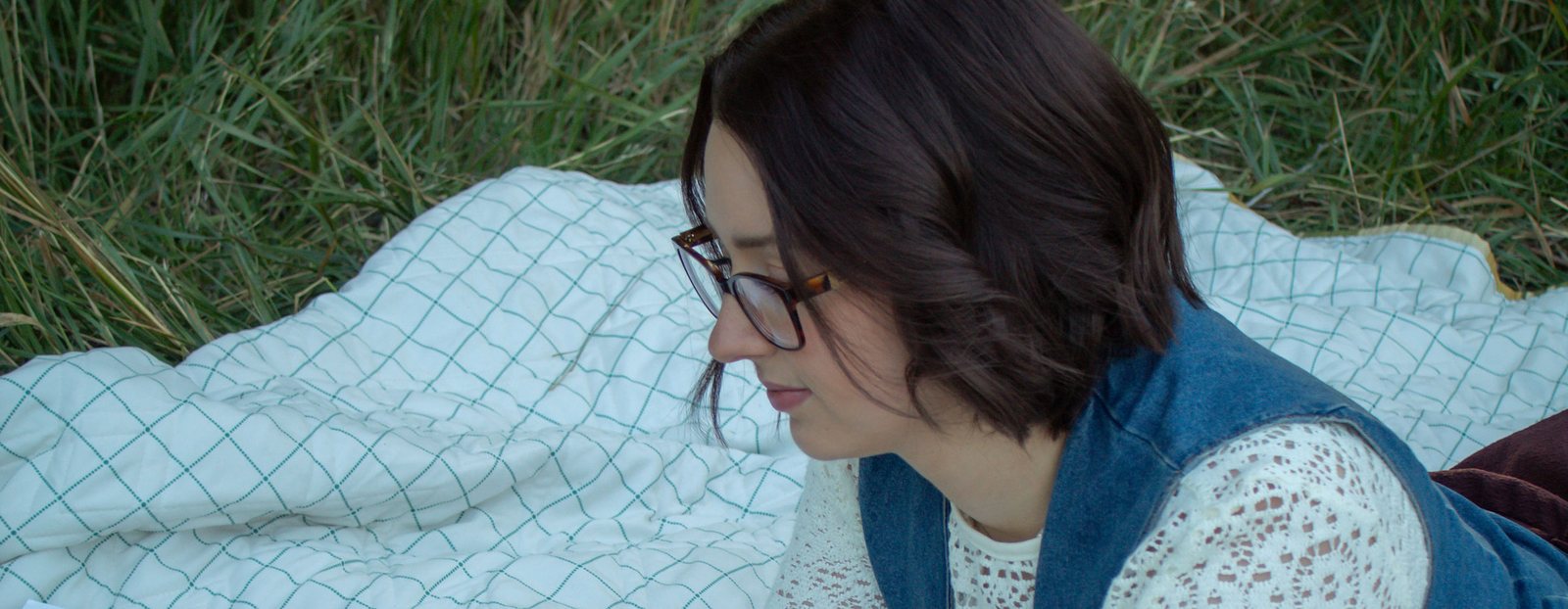 Lynea Millward writing on a laptop on a quilt in the grass